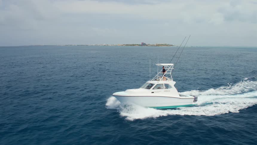 A person on a boat in the ocean with land the sky and clouds in the background