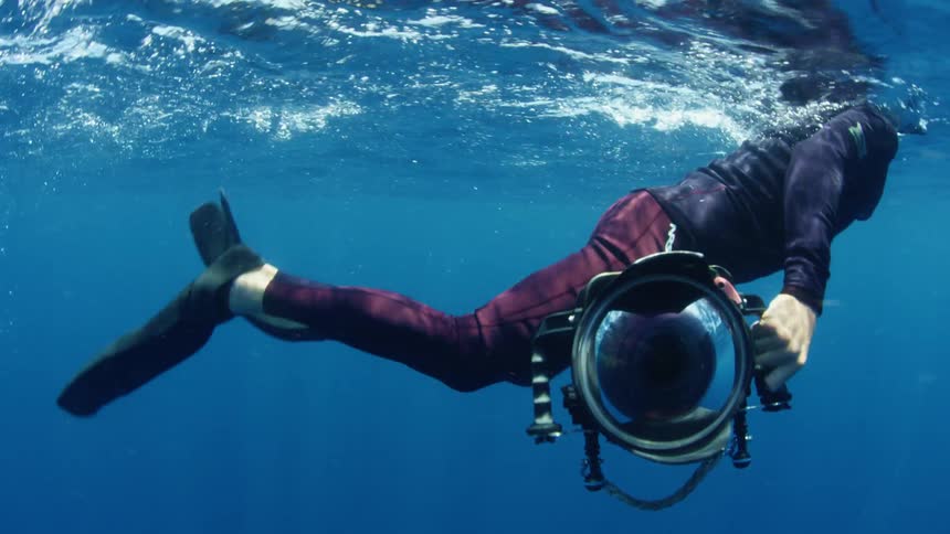 Free diver holding an underwater camera swims on the blue ocean waters