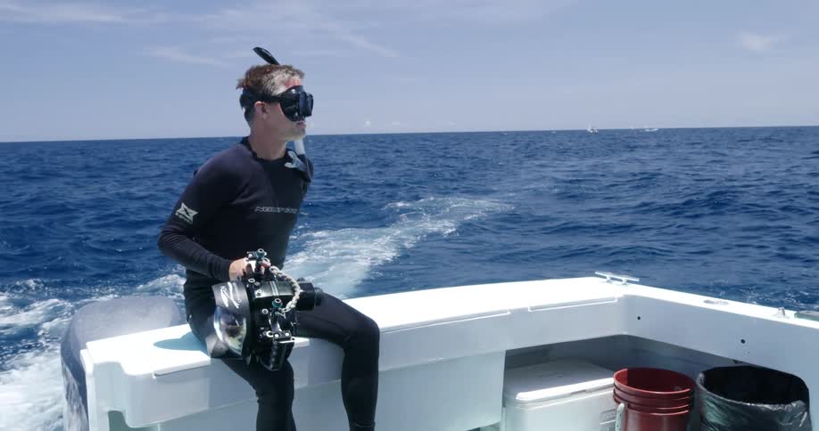 A scuba diver waves while riding on the back of a boat on the open ocean