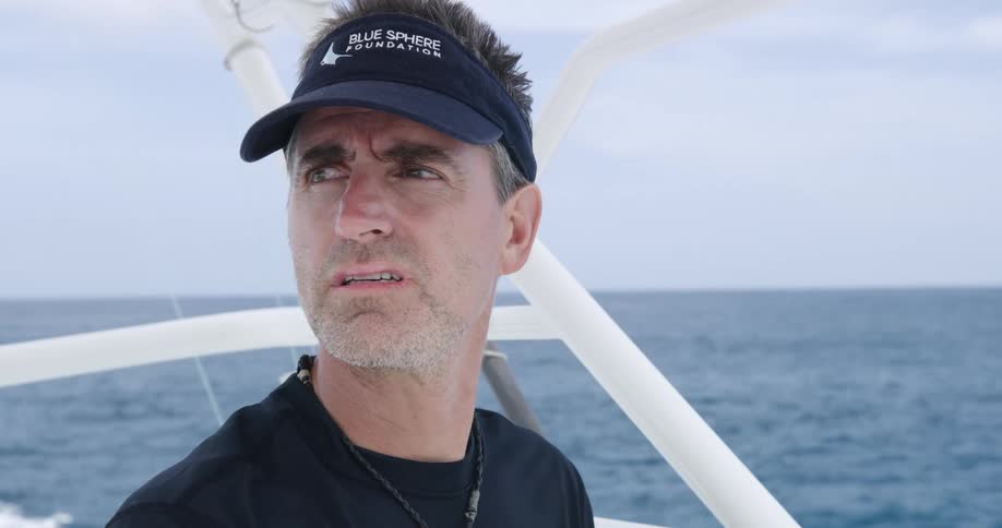 A man steering a motorboat scans the ocean in front of him with a look of concern on his face