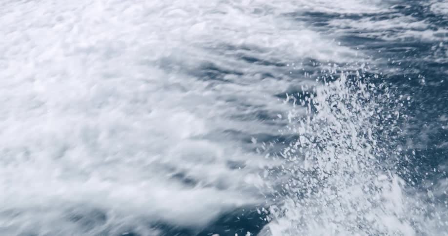 Waves and foam on the surface of the ocean water in the wake of a yacht