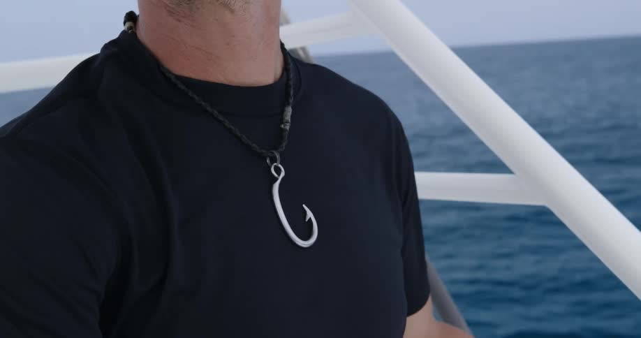 A man wears a fish hook necklace while sailing on the open sea