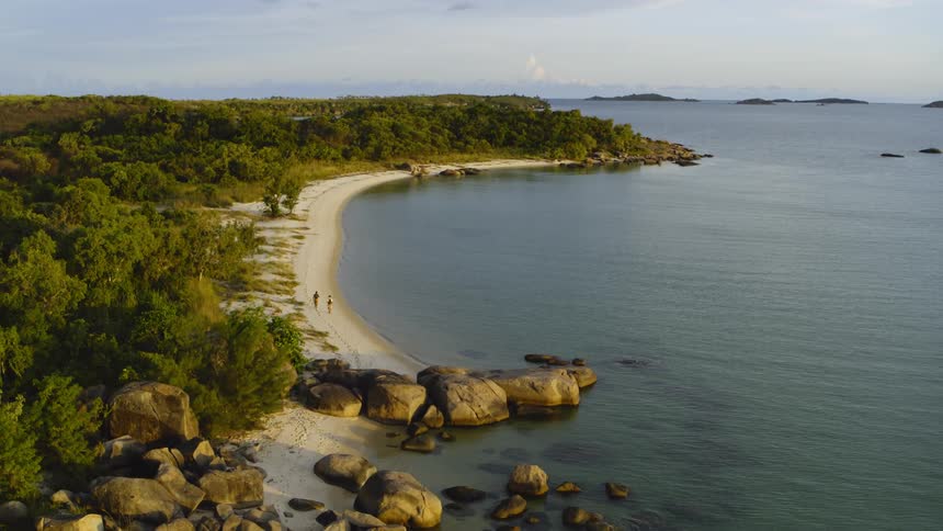 Aerial view of two man walking on the sand of a beach in a tropical island