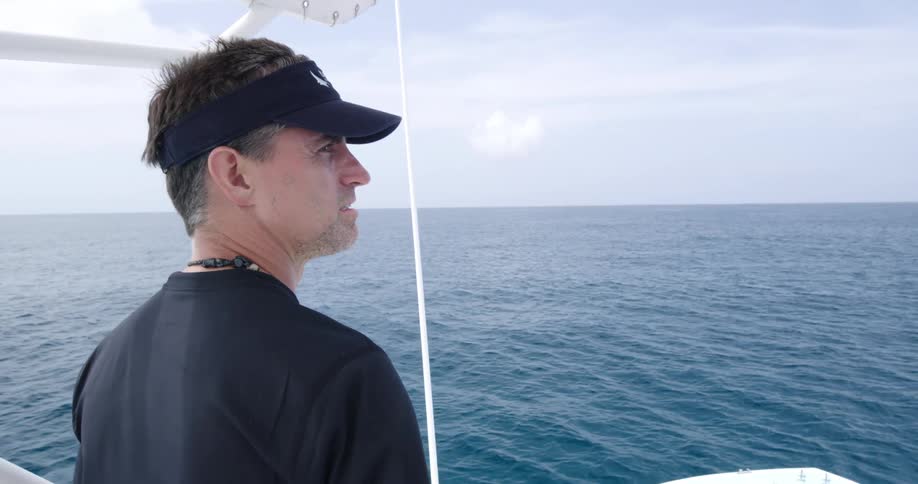 A man stands on a boat and looks out at the ocean