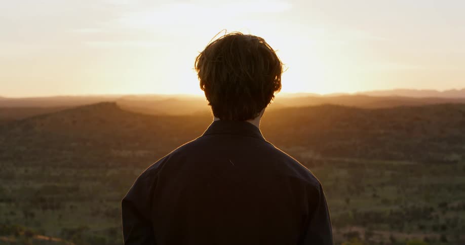 Man with a dark shirt stands and watches sunset on the edge of a cliff