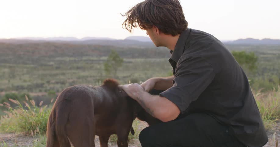 A man is outdoors and petting his dog