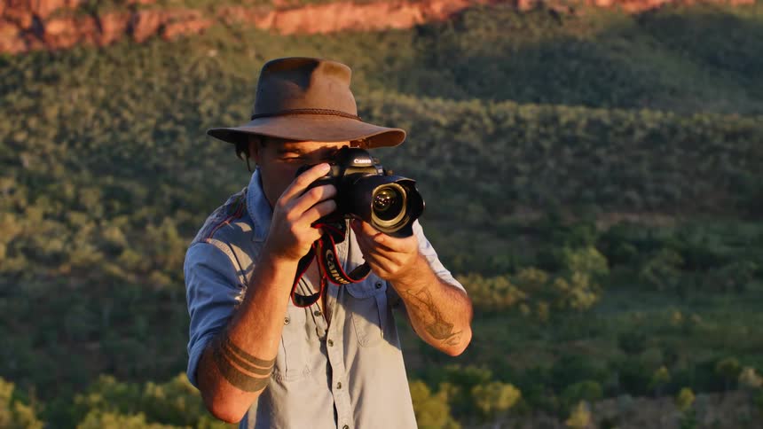 A male photographer shields his eyes with his hand from sunlight before attempting to take a photo