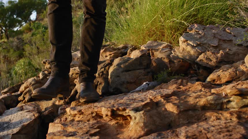 Person wearing leather boots walks over the rocks on a hill at sunset
