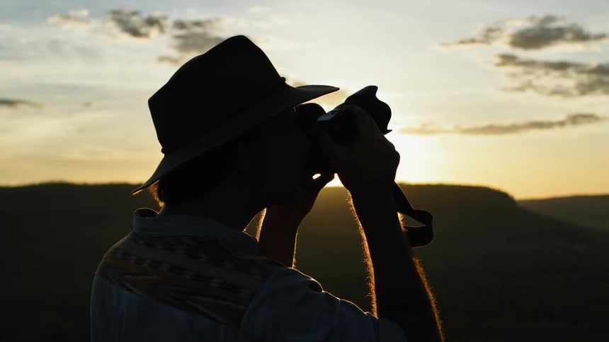 A man is standing outdoors and taking pictures with a camera