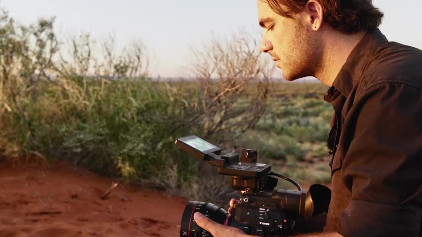 A man records an interview with a woman in the desert