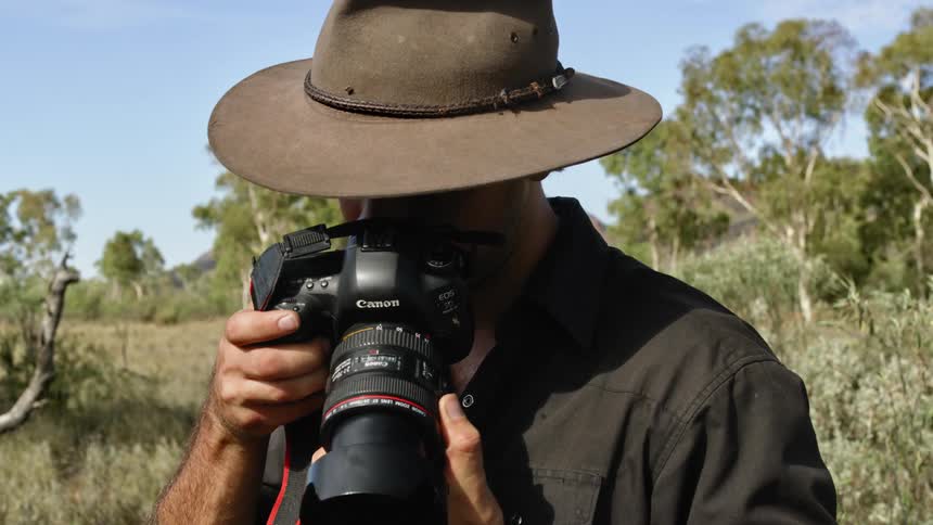A photographer uses a camera to take a photograph while flies buzz around him