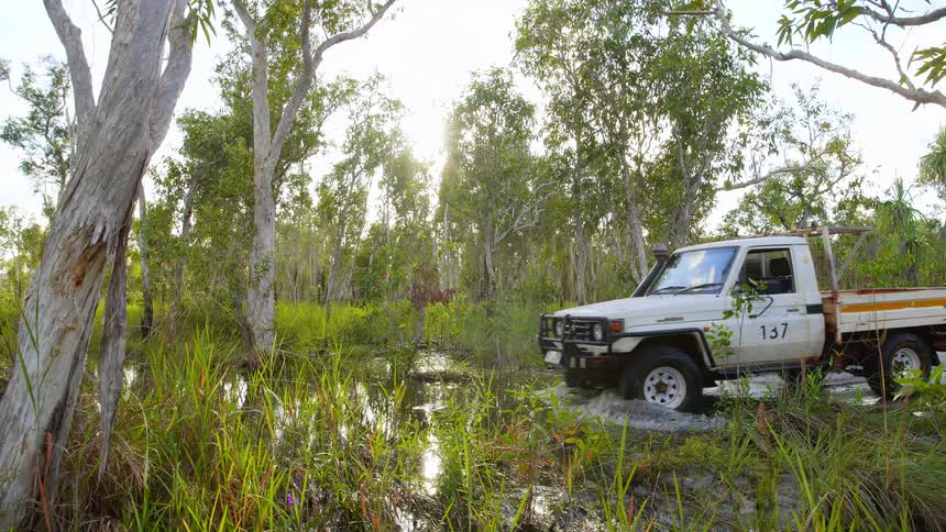 All terrain vehicle drives on a flooded dirt road through the forest