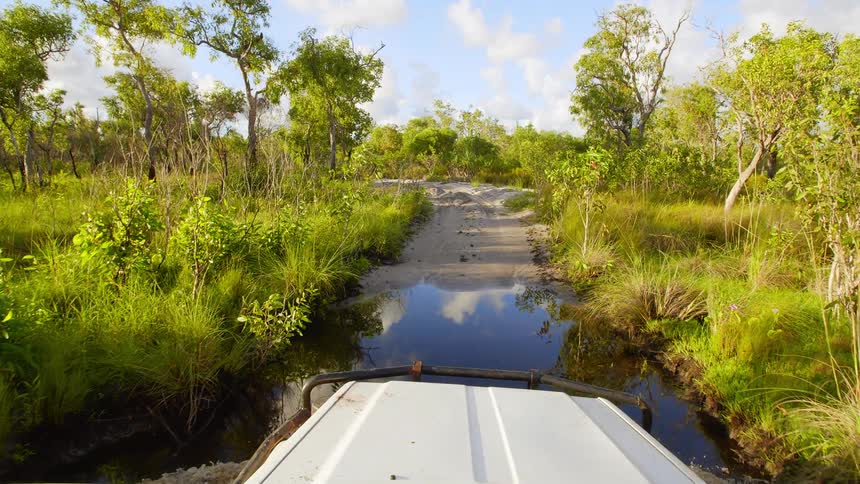 A car drives over a flooded dirt road in nature
