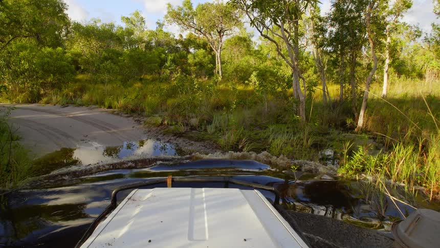 All terrain vehicle drives through a flooded section of a road through the forest