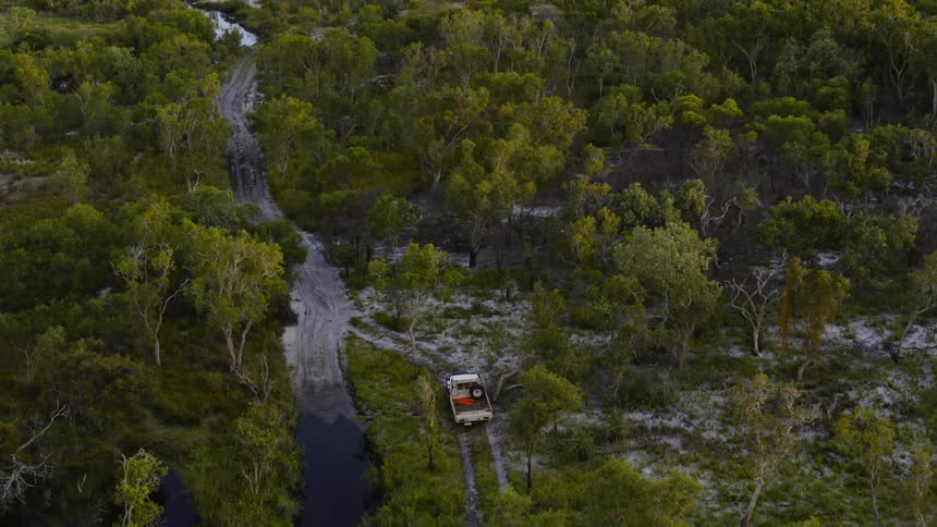 A truck drives a dirt road path in the woods towards a body of water