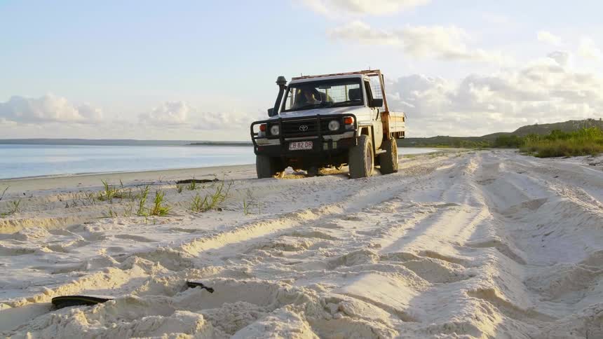 A person is driving a truck near the coast of a beach
