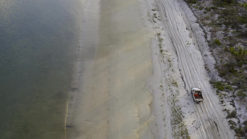 A white truck drives on a sandy beach