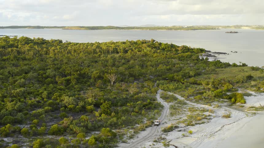 A car drives on a dirt road near a beach