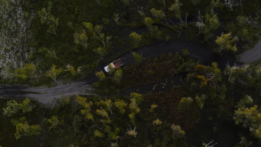 A truck drives through water on a flooded dirt road in a forest