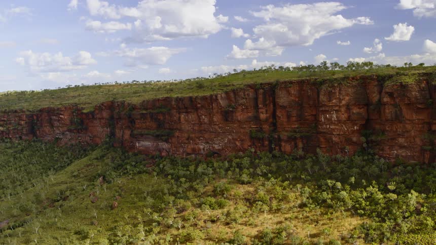 Aerial view of the red cliffs of a mesa surrounded by green trees and shrubs