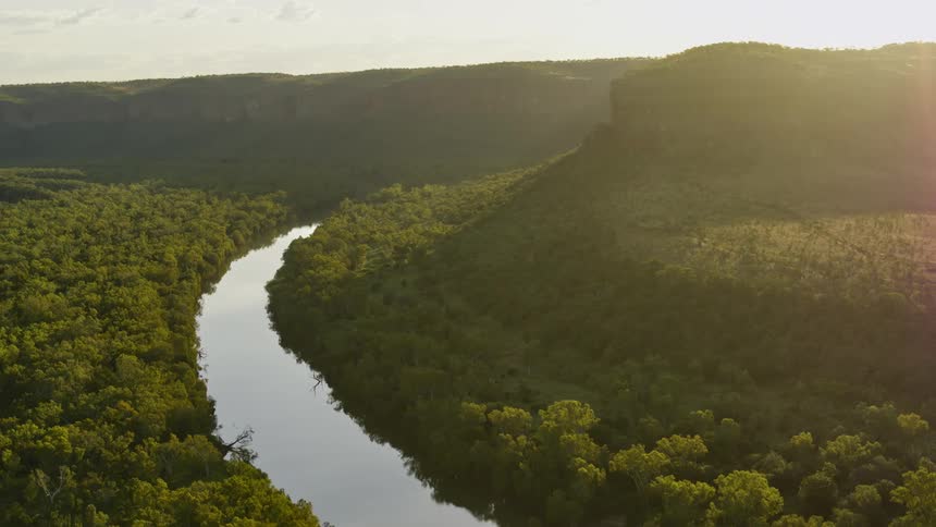 Sun shines over mountains as river curves through forest