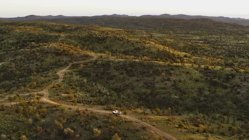 A truck travels along a dirt road through a hilly countryside