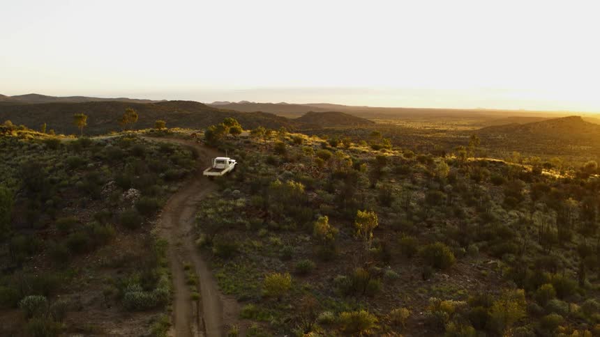 A truck travels along a dirt road through a hilly countryside