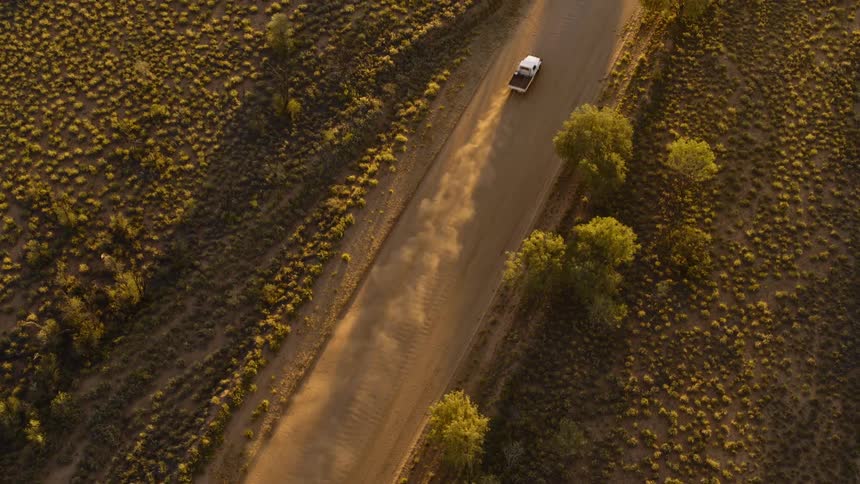 A white truck kicks up dust while driving on a rural dirt road