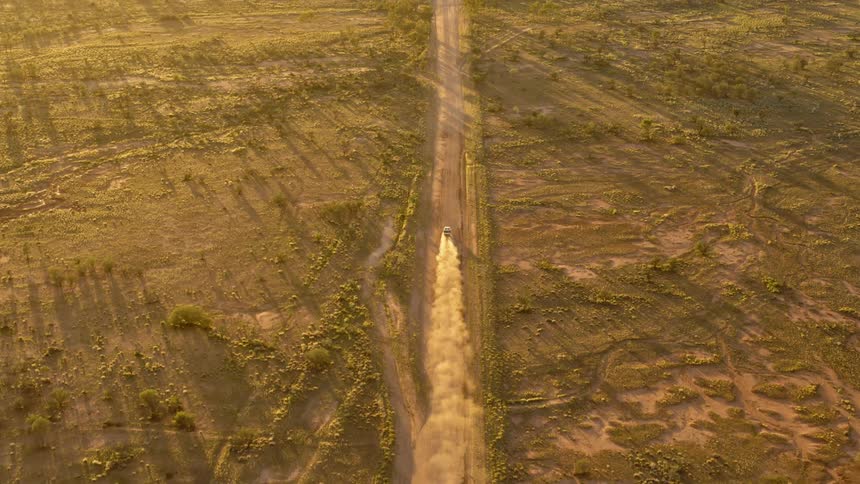 Aerial view of an all terrain vehicle driving on a dirt road through the desert at sunset