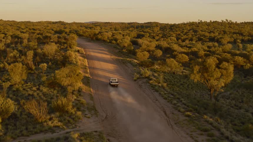 A truck speeding down a dirt road through a vast hilly countryside