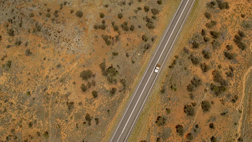 Aerial view of a car driving on a rural road through the desert