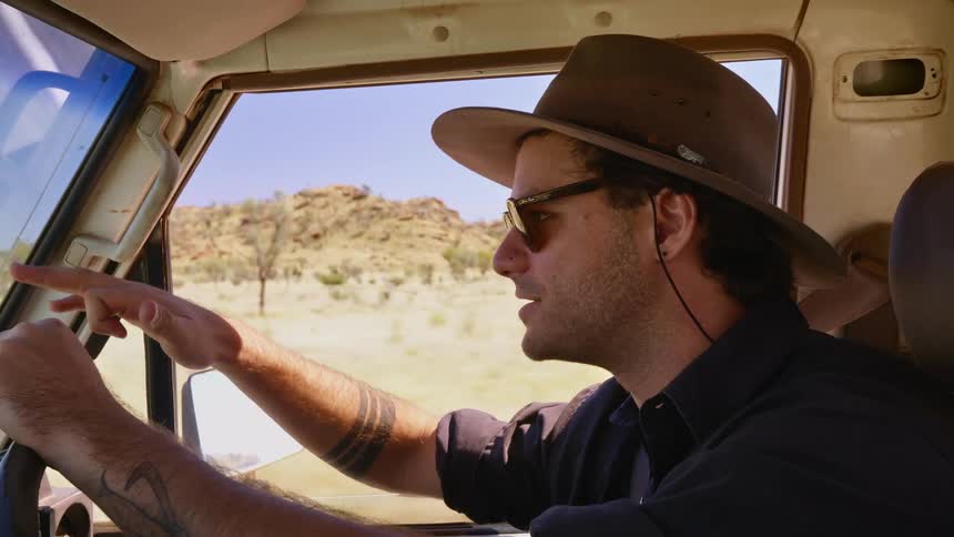 Man wearing hat and sunglasses drives a truck on a desert road