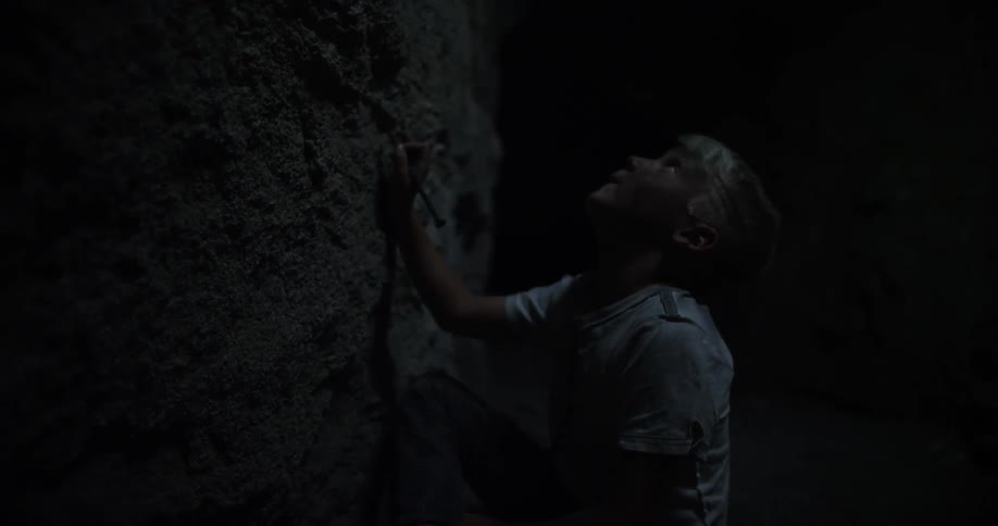 A boy writes on a rock wall with a stick