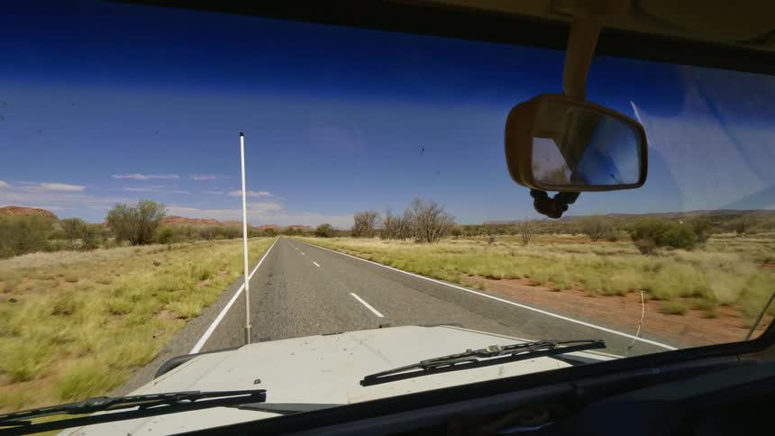 A truck travels down a road through a vast grassland on a sunny day