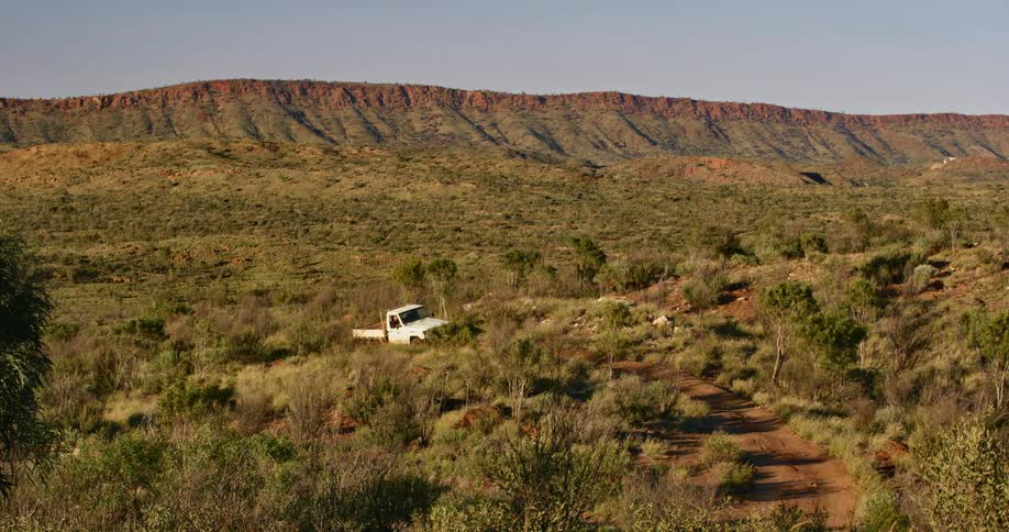 Truck driving on a dirt road through the bushes and shrubs near the mountain