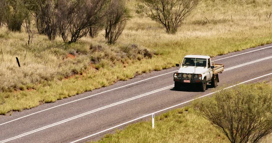 White pickup truck drives on a highway seen from a hill