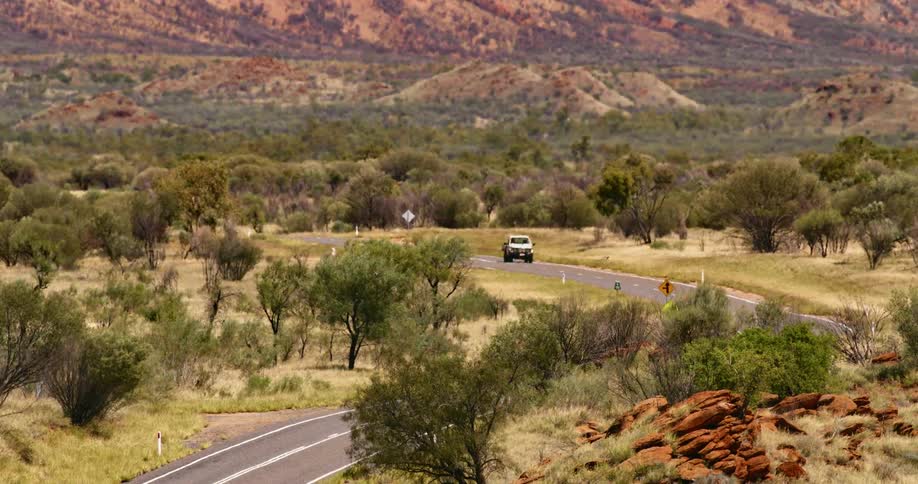 A vehicle travels along a road through a vast grassland