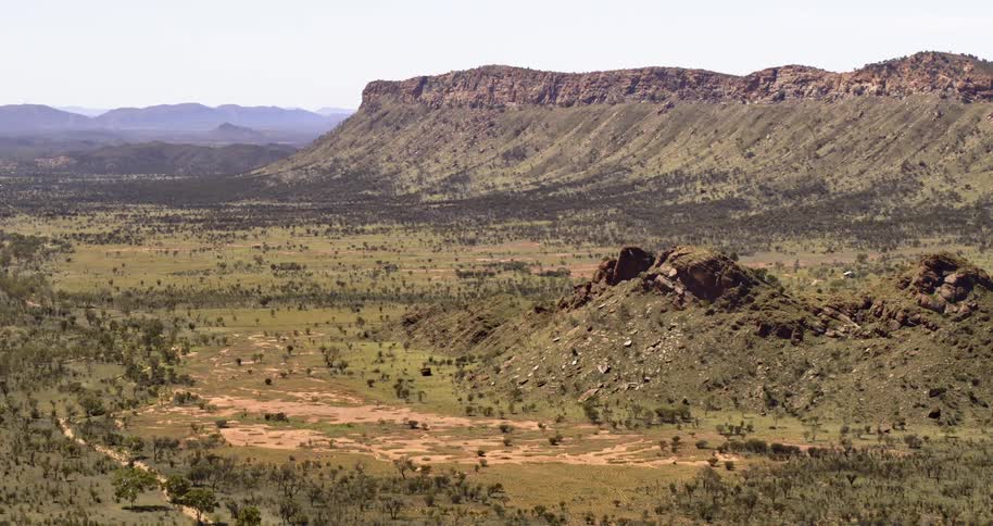 A vast grassland between a brown stone mountain ridge on a sunny day