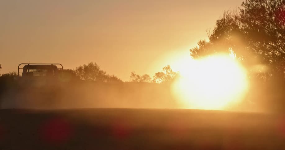 The sun setting as a truck drives over a dirt road