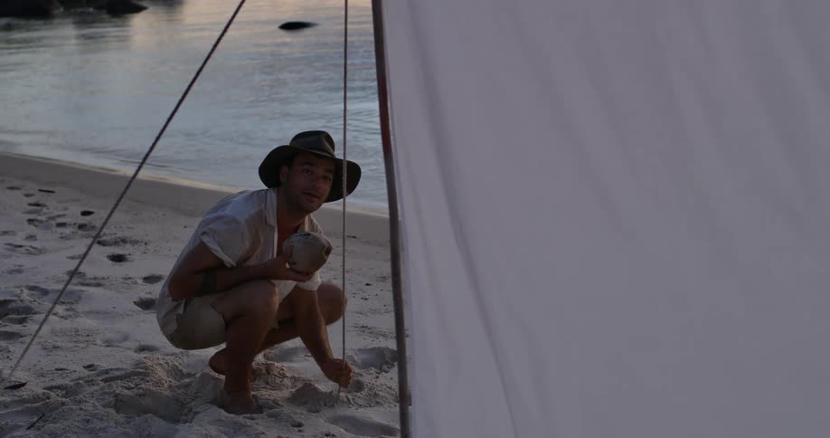 A man adjusting a rope holding up a makeshift shelter on the beach