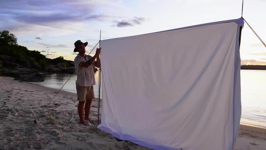 A man fixes a sheet attached to some rope on the sandy beach