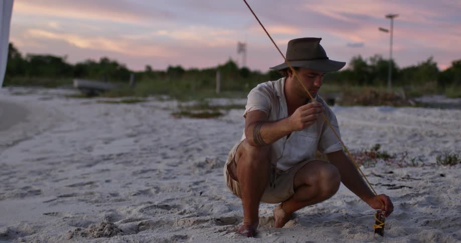 A man on a beach secures a rope around a stick on a beach