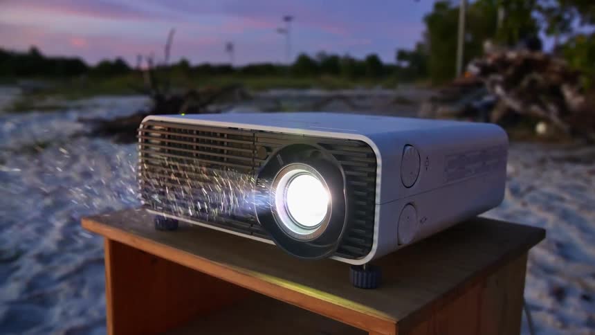 Projector on a table over the sands of a beach beaming light at sunset