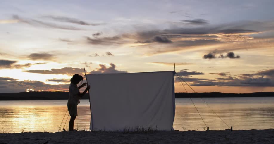 Person setting up a screen on the shoreline near the lake at dusk