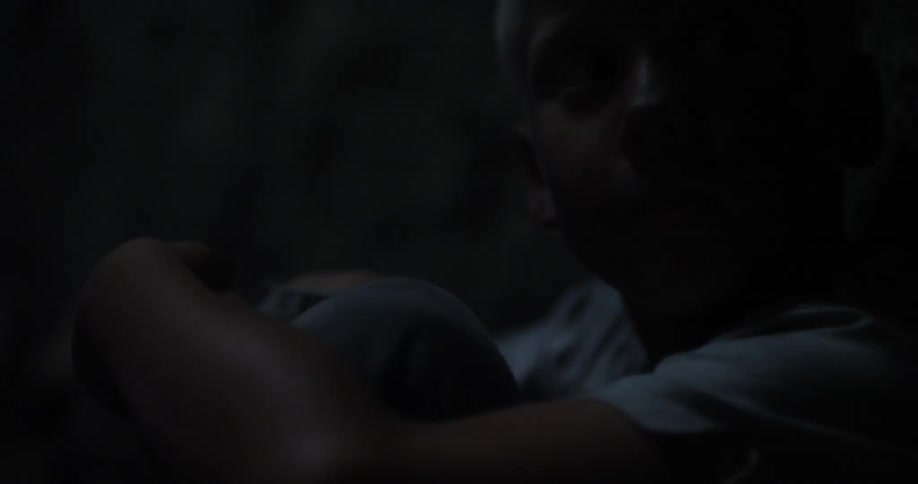A boy with his arms wrapped around his legs lifts his head