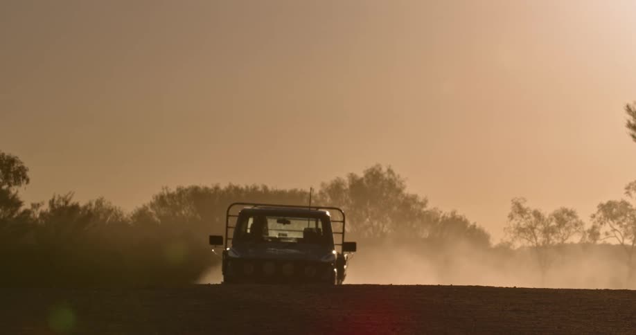 Truck drives along dirt road through amber tinted day kicking up dust