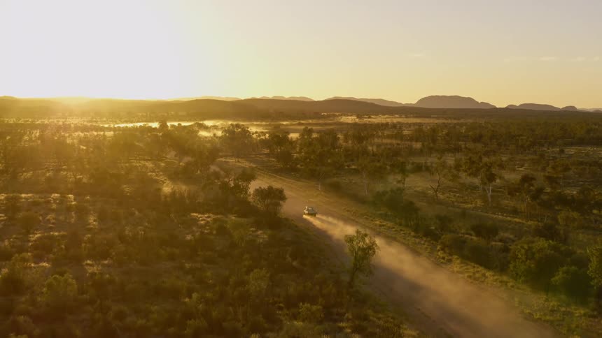 Vehicle travels on a dirt road near the trees stirring up dust
