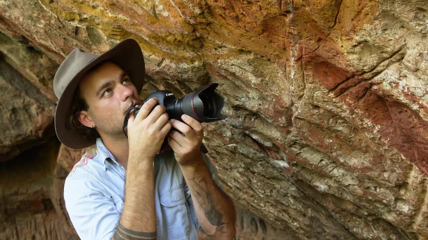 A man is taking photos of a cliff outdoors