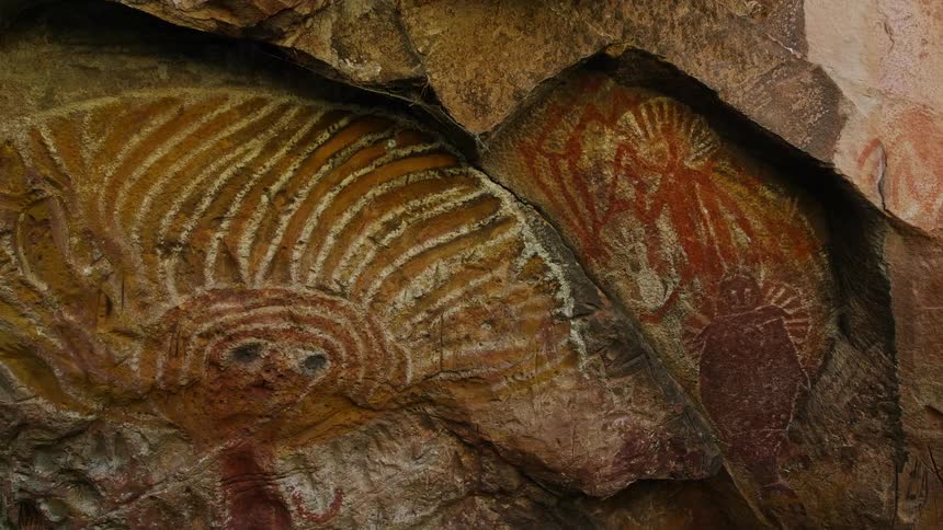 On the surface of a rock wall is a prehistoric looking cave drawing