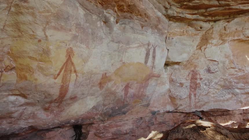 A young man hiking with a camera comes up to stones with drawings on them